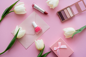 top view of white tulips near envelope, gift box and decorative cosmetics on pink