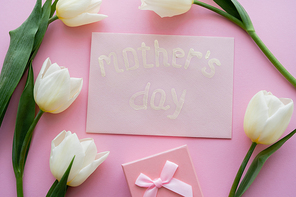 top view of envelope with mothers day lettering near gift box and white flowers on pink
