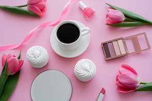 top view of cup with coffee near zephyr, decorative cosmetics and tulips on pink