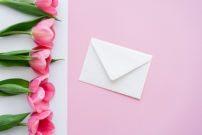 top view of envelope near blossoming tulips on white and pink