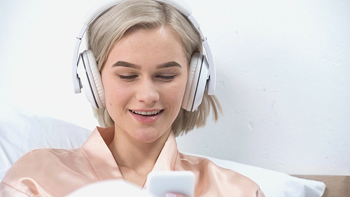 cheerful young woman in wireless headphones listening music and using smartphone