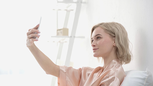 cheerful blonde woman taking selfie on smartphone