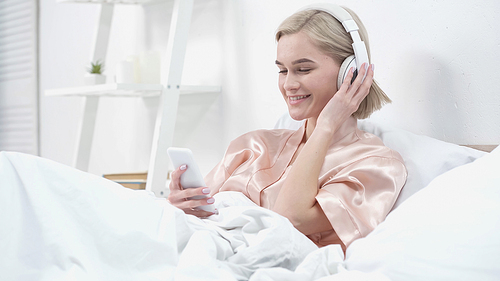 happy young woman in wireless headphones listening music and using smartphone