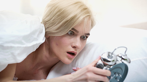 shocked young woman looking at retro alarm clock in bedroom