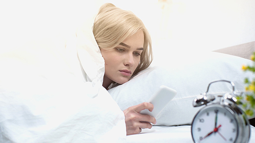 awake woman using smartphone near retro alarm clock