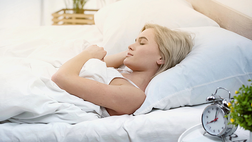young blonde woman with closed eyes sleeping in bedroom