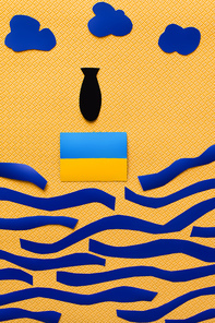 Top view of paper bomb near Ukrainian flag, clouds and carton sea on textured yellow background