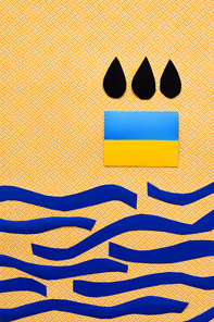 Top view of black drops above ukrainian flag and paper sea on textured yellow background