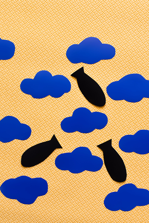 Top view of paper bombs near carton clouds on textured yellow background, war in ukraine concept
