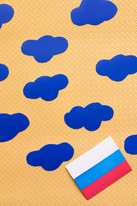 Top view of russian flag and paper clouds on textured yellow background, war in ukraine concept