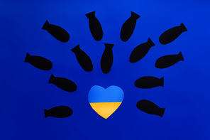 Top view of paper bombs above ukrainian flag in heart shape on blue background