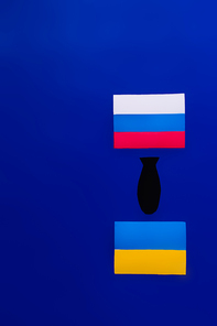 Top view of paper bomb between russian and ukrainian flag on blue background