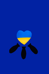 Top view of paper bombs under ukrainian flag in heart shape on blue background