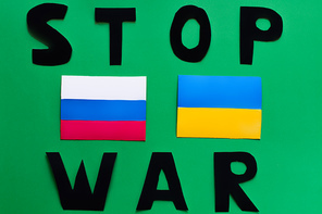 Top view of stop war lettering and ukrainian and russian flags on green background