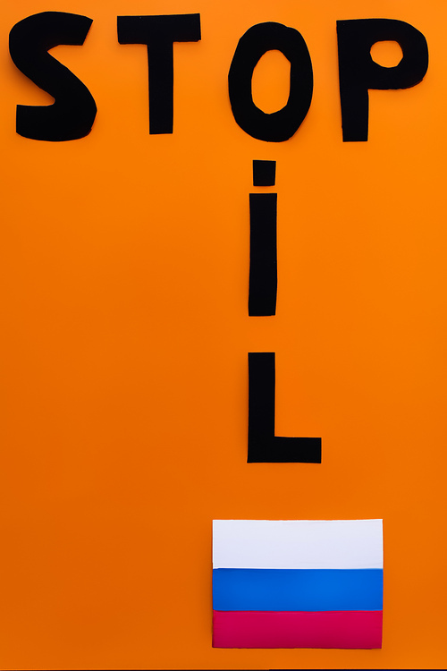 Top view of stop and oil lettering near russian flag on orange background