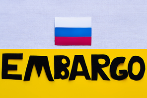 Top view of russian flag and embargo lettering on white and yellow background