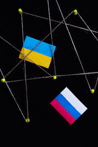 Top view of ukrainian and russian flags near push pins with thread isolated on black