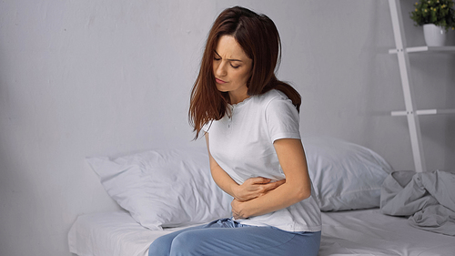 woman sitting on bed and hugging belly while feeling abdominal pain