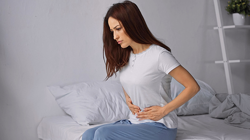 brunette woman touching belly while feeling abdominal pain in bedroom