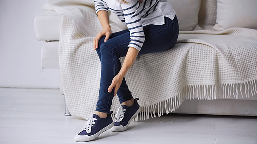 partial view of woman sitting on couch and touching painful leg