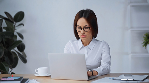 brunette woman in eyeglasses working at laptop in office
