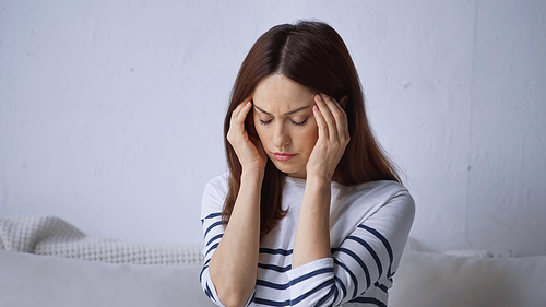 exhausted woman with migraine touching head while sitting at home