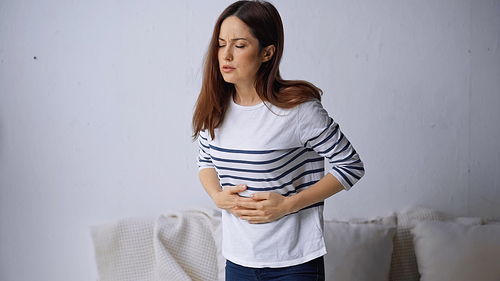 brunette woman standing with closed eyes and suffering from abdominal pain