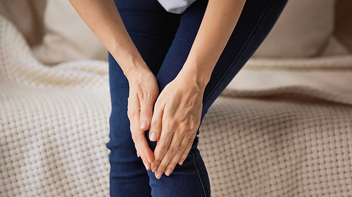 cropped view of woman touching painful knee while standing at home