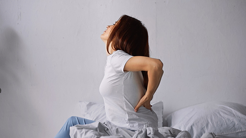 side view of woman suffering from pain in back while sitting on bed