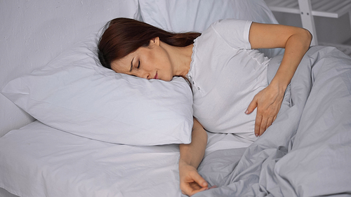 brunette woman feeling pain in stomach while lying on bed