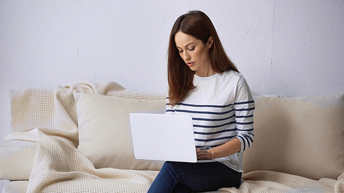 brunette woman sitting on couch at home and working on laptop