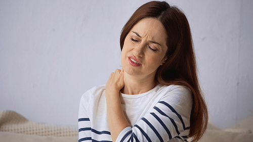 brunette woman frowning with closed eyes while suffering from neck pain
