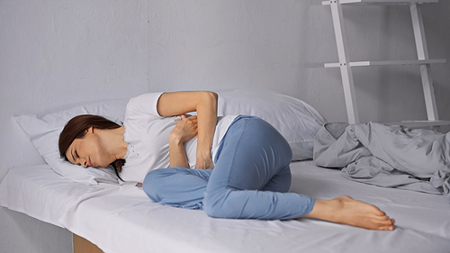 woman lying on bed in pajamas and suffering from abdominal pain