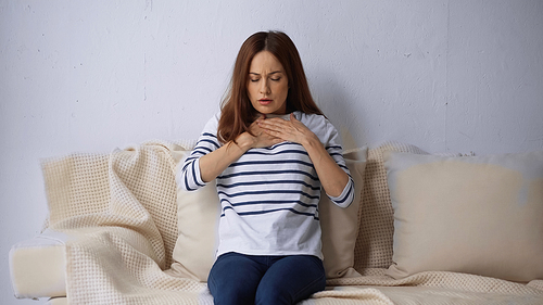 woman with closed eyes sitting on couch and feeling pain in chest