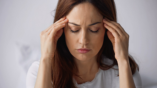 brunette woman with closed eyes touching head while suffering from migraine on grey background