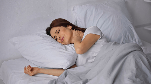 brunette woman lying on bed with closed eyes and touching painful neck