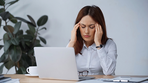 businesswoman with closed eyes touching head while suffering from migraine at workplace