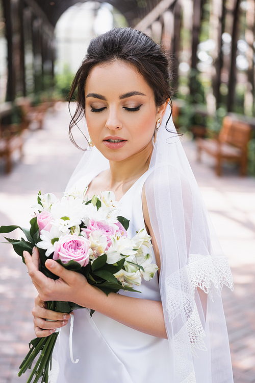 Pretty bride holding wedding bouquet outdoors