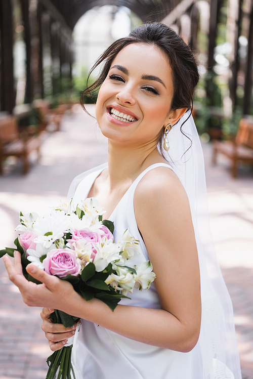 Happy bride holding wedding bouquet in park