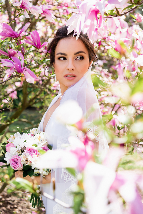 Bride with bouquet looking away near blooming magnolia tree