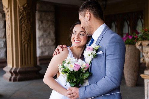 Groom embracing happy bride with bouquet outdoors
