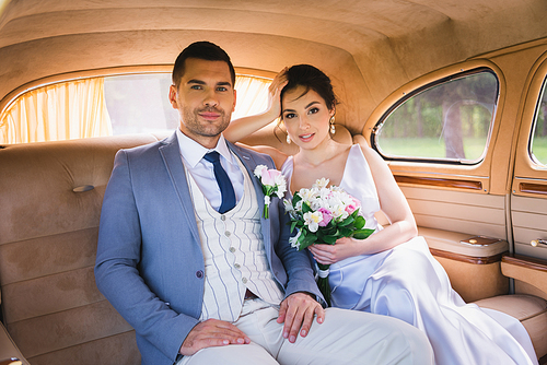 Smiling bride with bouquet  near groom in vintage car