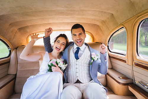 Excited newlyweds showing yes gesture in vintage car