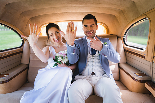 Blurred newlyweds showing rings in retro car