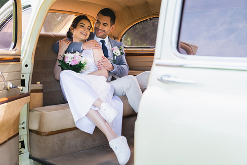 Smiling groom embracing bride in vintage car