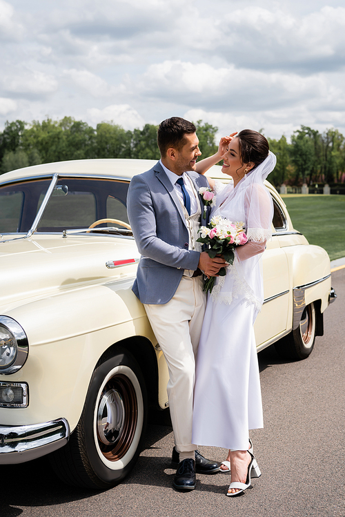 Side view of smiling newlyweds standing near vintage car