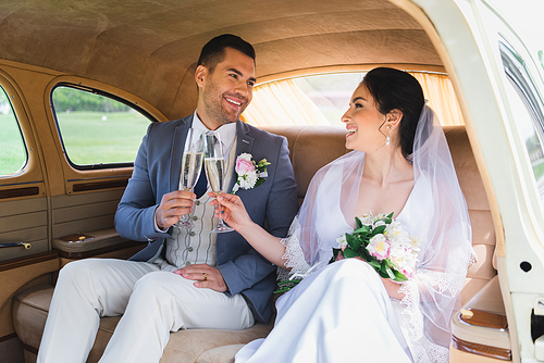 Happy bride and groom clinking with champagne in vintage car