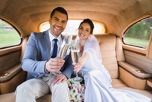 Blurred newlyweds holding glasses of champagne in retro car