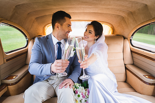 Smiling newlyweds looking at each other while toasting with champagne in car