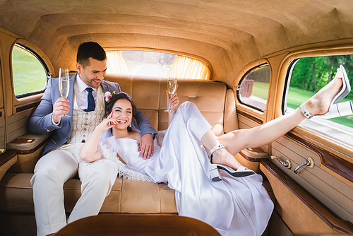 Positive newlyweds holding champagne in retro car